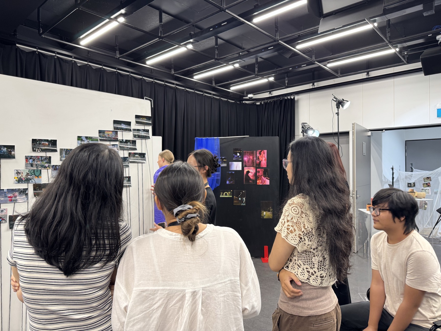 Visitors moving among the black-curtained booths of the re-root exhibition in the Media Studio